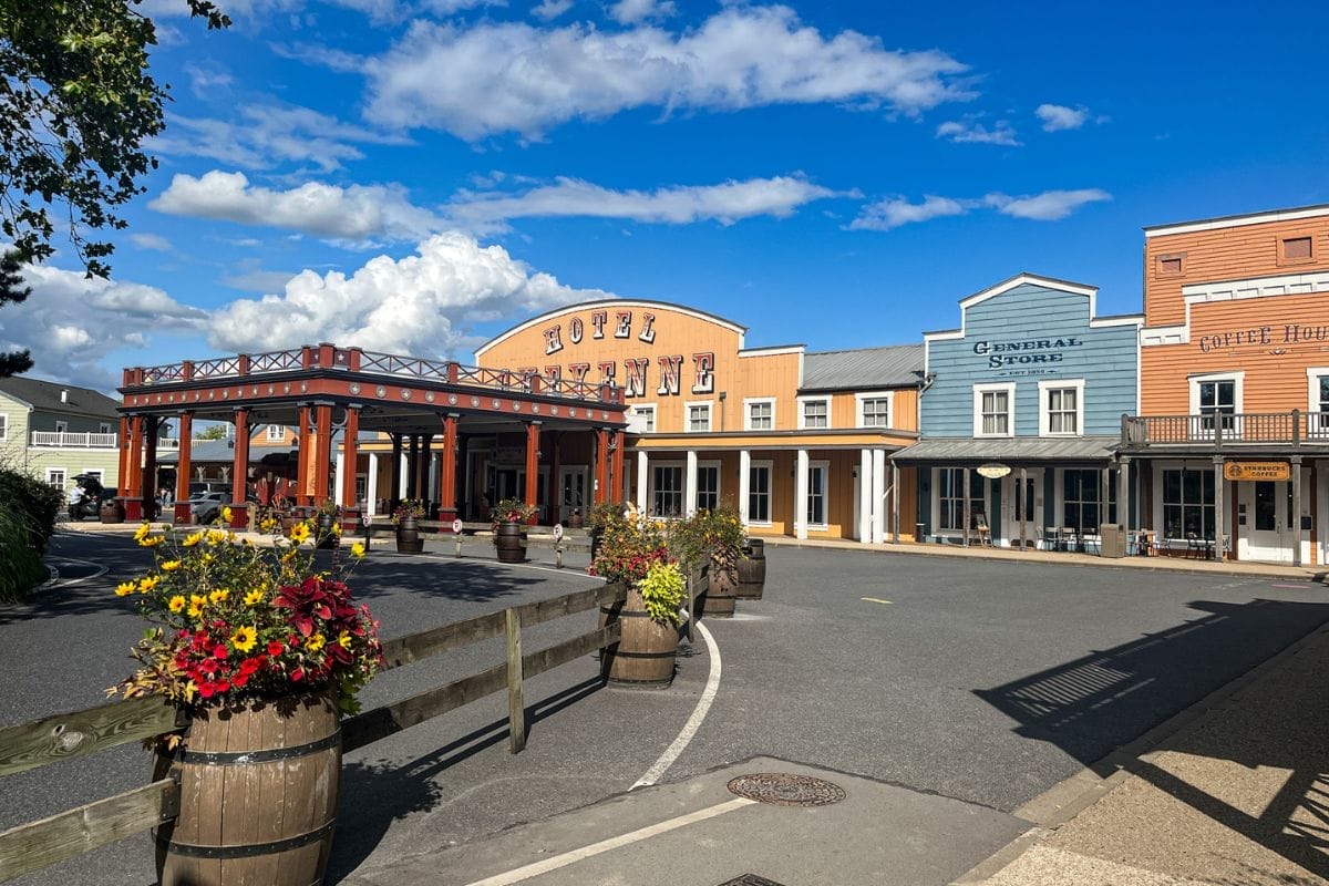 The entrance to Hotel Cheyenne at Disneyland Paris, styled like a Western town with a prominent sign, flower barrels, and colorful wooden facades under a partly cloudy sky.