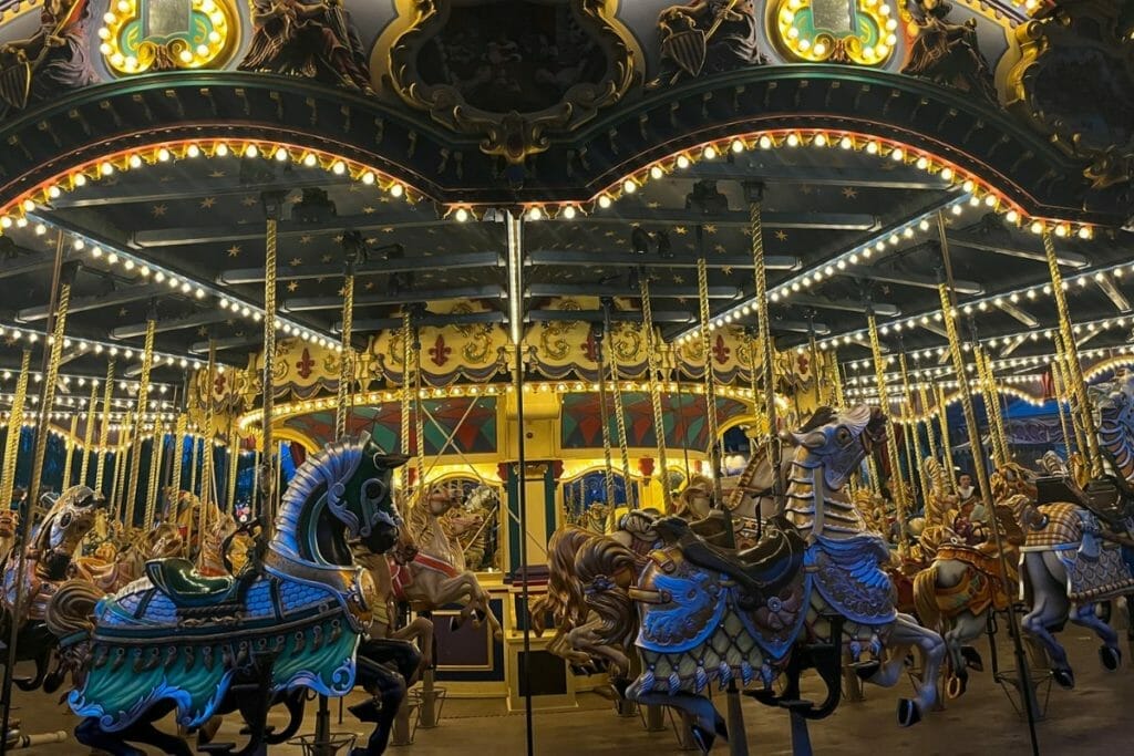 A brightly lit carousel at Disneyland Paris, filled with ornately decorated horses and riders, illuminated by numerous twinkling lights against a night sky.