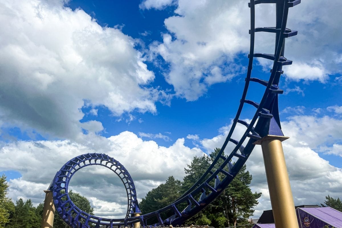 A blue roller coaster track at Legoland Windsor with a loop against a backdrop of a bright blue sky and fluffy white clouds.