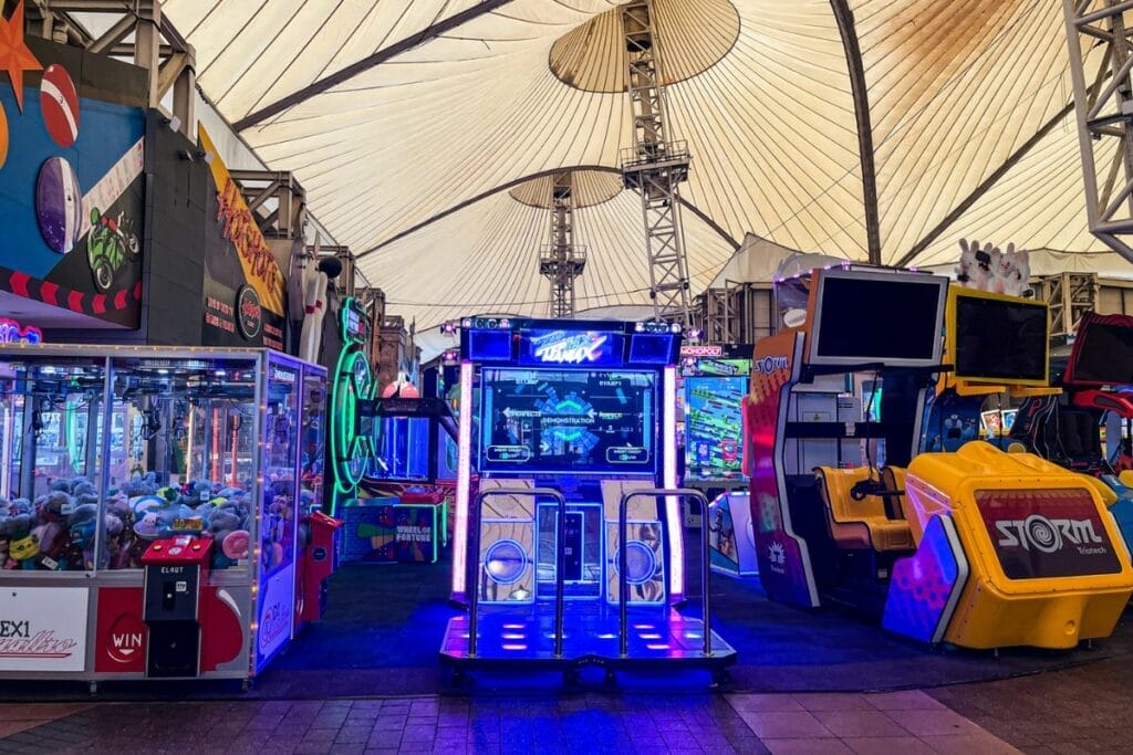 The interior of the Butlins Minehead arcade, filled with vibrant, neon-lit arcade machines. Plush toy claw machines and video game setups create a lively and inviting atmosphere under a large tent-like structure.